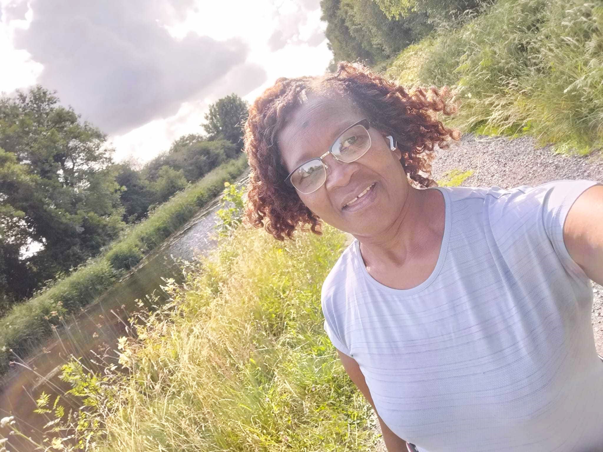 Yanai walks along a path by a river, with the sun shining behind her.